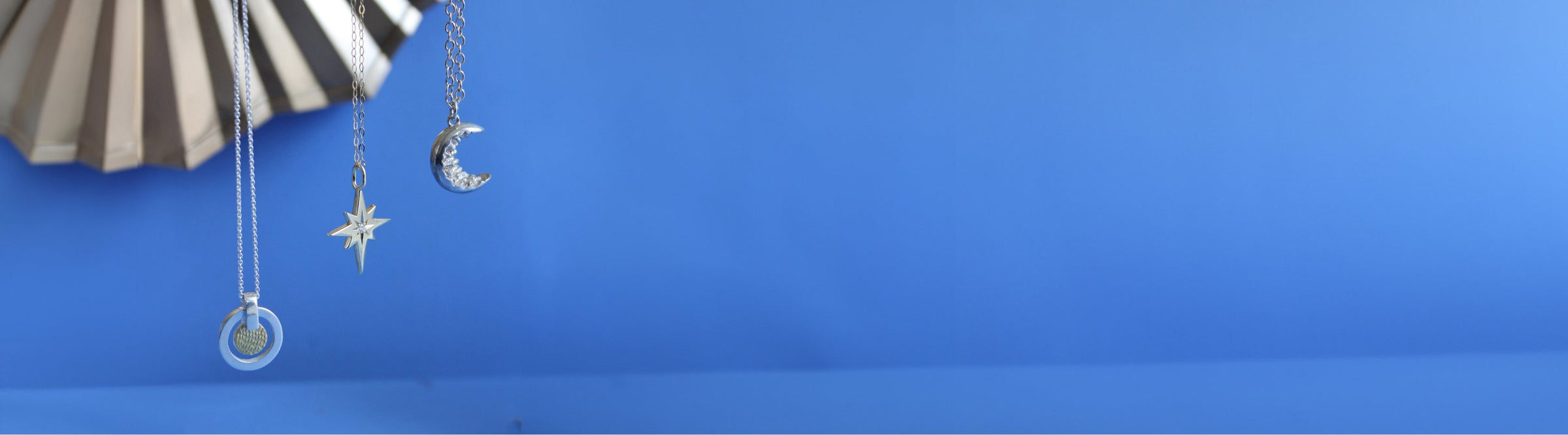 A blue background with three necklaces hanging: one with a star pendant, one with a crescent moon pendant, and one with a round pendant. The word "Necklaces" is written at the bottom.