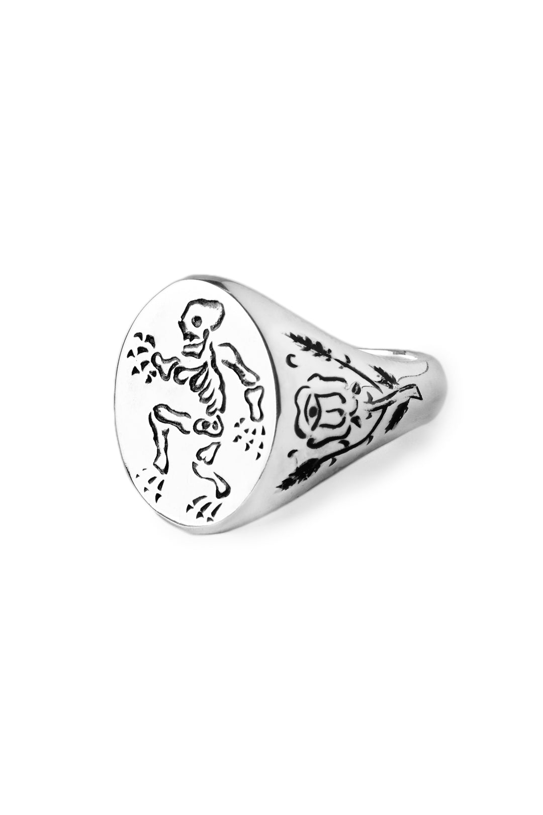 The Sterling Silver Memento Mori Signet Ring by Cosmic Boulevard features a skeleton and scattered dots on the face, plus a trident symbol and ornate detailing on the side.