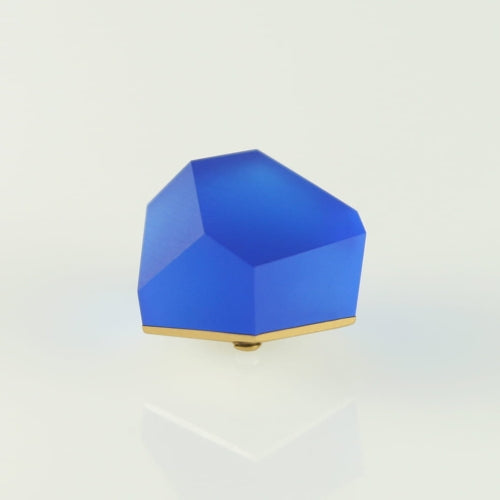 A Fruit Bijoux Fruit Bijoux Ring Top VU Crystals Cobalt Blue with a 24ct gold-plated base resting on a reflective, white surface. The object has a modern, abstract design and appears to be a sculpture or decorative item.