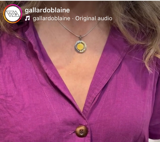 A person wearing a bright purple button-up shirt and the Gallardo & Blaine Designs Urú Small Pendant & Chain. The photo is cropped to show only the neck, collar, and upper chest area.