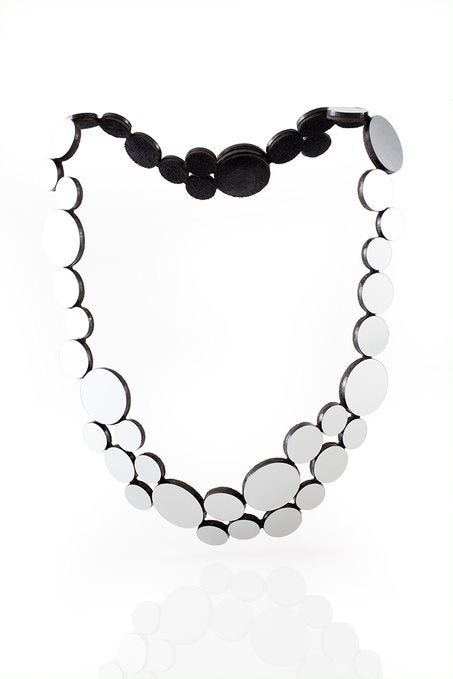 A stylish Abstraction Fizz Silver Necklace featuring multiple, gradually increasing silver circles arranged in a symmetrical pattern. The circles are connected by black links, creating an elegant and modern design against a plain white background. This lightweight jewelry piece is one of Iskin Sisters' designs.