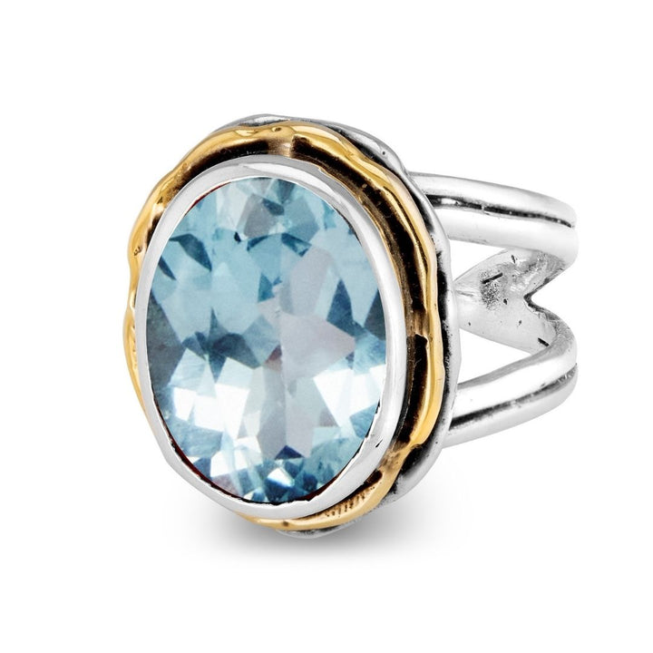 The Magnolia Ring by Gallardo & Blaine Designs features a large, oval-cut light blue gemstone set in a gold-accented sterling silver bezel with an open split shank band.
