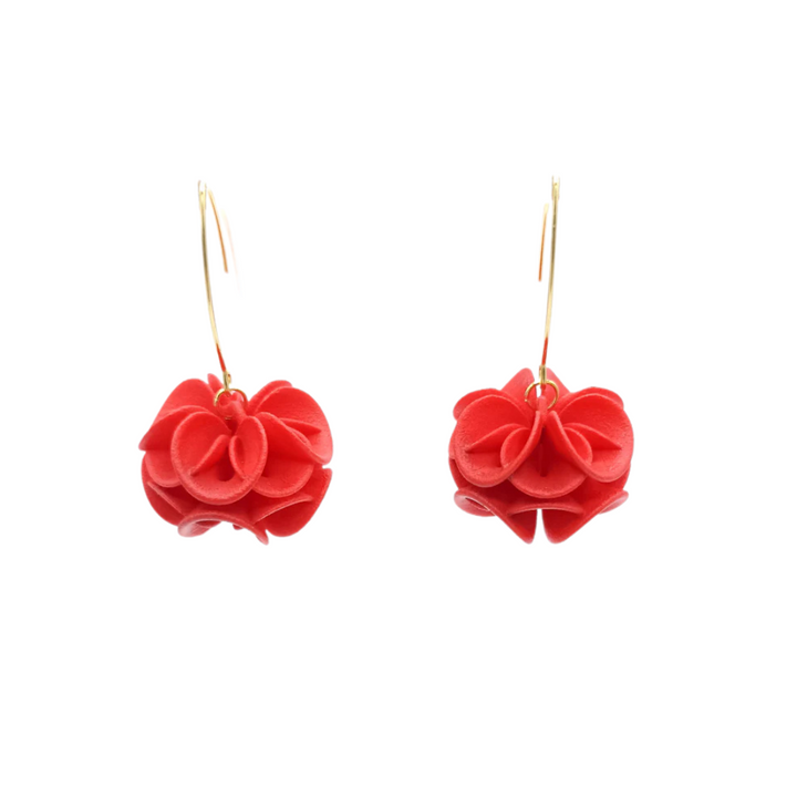The Tochu-De Red Rose Earrings feature red, flower-shaped pendants on thin gold hoops, elegantly displayed against a white background.