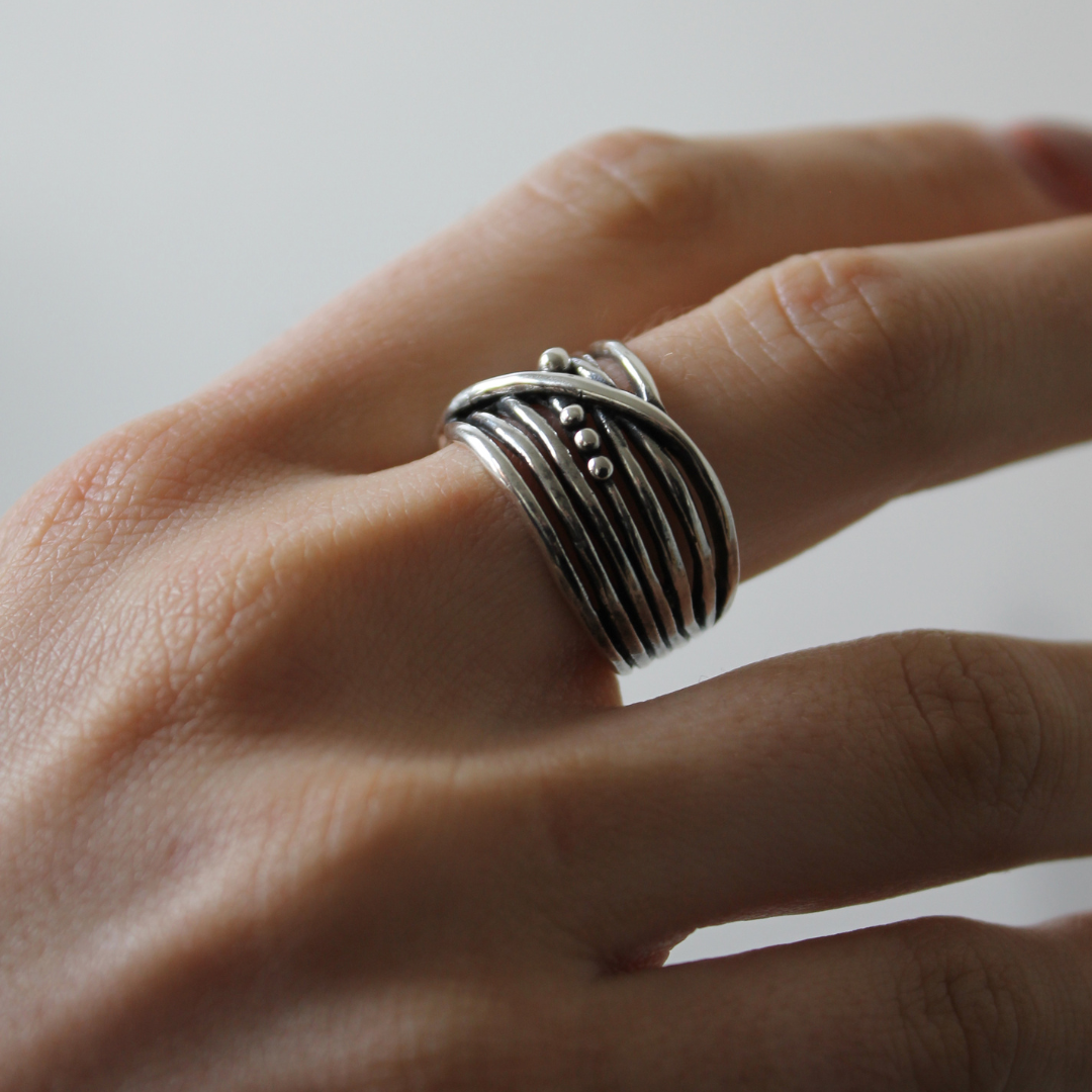 A close-up of a hand wearing the Bamboo Ring in Sterling Silver & Gold Vermeil by Gallardo & Blaine Designs, featuring wavy, overlapping bands and small decorative silver dots. The plain background is softly blurred.