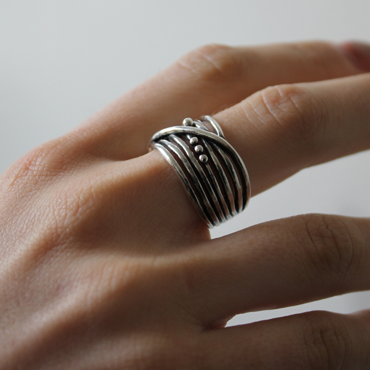A close-up of a hand wearing the Bamboo Ring in Sterling Silver & Gold Vermeil by Gallardo & Blaine Designs, featuring wavy, overlapping bands and small decorative silver dots. The plain background is softly blurred.