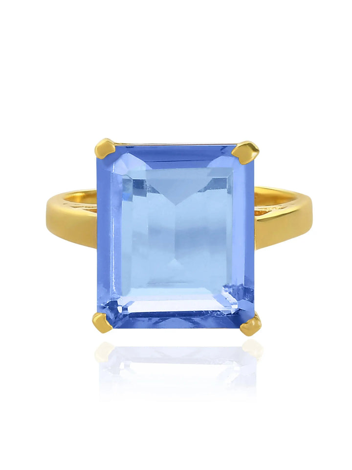 The Claudia Ring by Shyla is a vintage-inspired gold chunky ring with a large, emerald-cut light blue gemstone in a four-prong setting, shown on a white background.