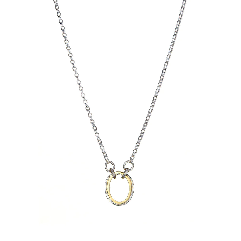 A delicate silver chain necklace with a small, circular pendant at the center. The pendant has a gold-toned inner circle and a silver-toned outer edge, creating a simple yet elegant design. Paired perfectly with matching Carran Mix Pendant earrings by Lynsey de Burca, the set is displayed against a clean white background.