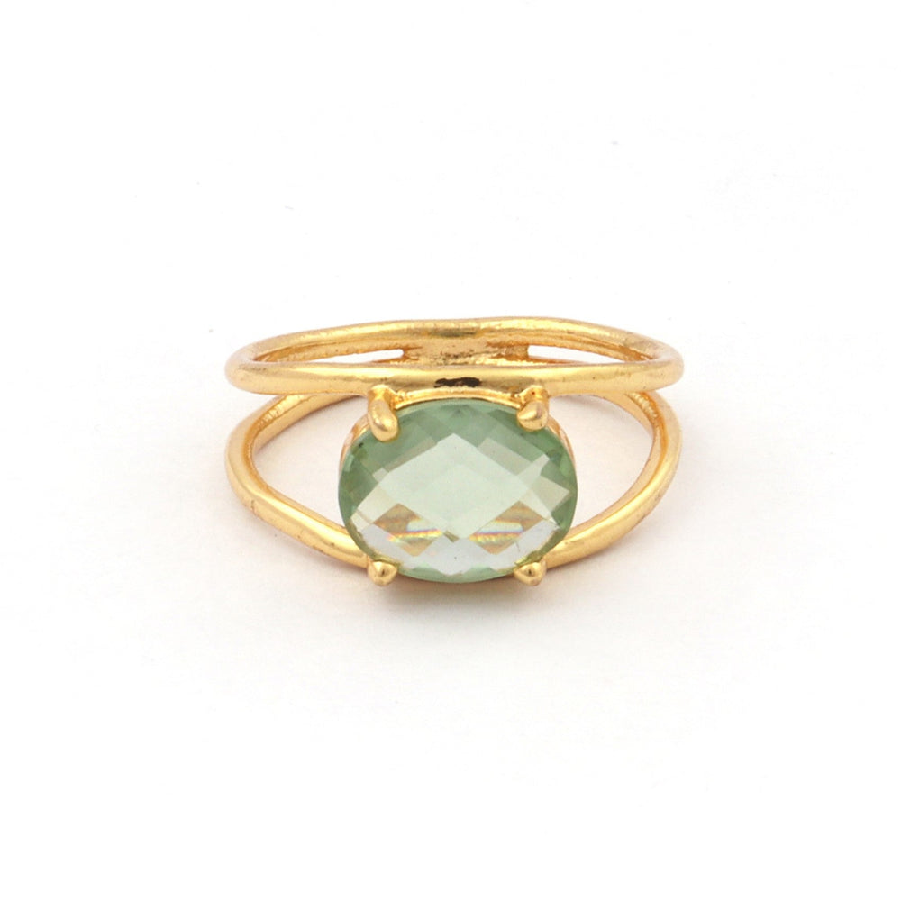 A gold-plated ring featuring a green Amethyst set in a four-prong setting. The ring's band, crafted from sterling silver, splits into two just below the gemstone, giving it a unique, open design. The Charlotte Gold Ring in Green Amethyst by Watermelon Tropical is displayed against a plain white background.