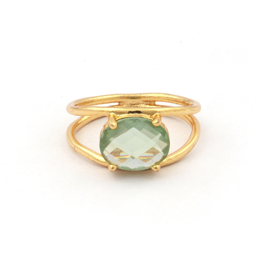 A gold-plated ring featuring a green Amethyst set in a four-prong setting. The ring's band, crafted from sterling silver, splits into two just below the gemstone, giving it a unique, open design. The Charlotte Gold Ring in Green Amethyst by Watermelon Tropical is displayed against a plain white background.