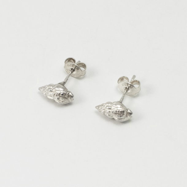 A pair of Whelk Shell Stud Earrings by Jennifer Kinnear, perfect for any shell collection. The earrings have a polished finish with intricate detailing to mimic the texture of real shells. They are placed on a white surface.