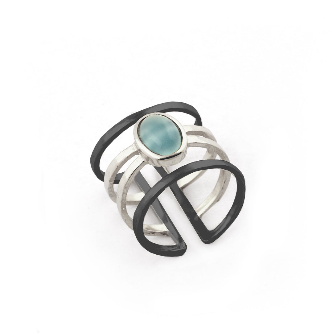Introducing the Andi Banded Ring in Amazonite by Watermelon Tropical—a contemporary piece crafted in sterling silver, showcasing a distinctive geometric design. This exquisite ring features a striking black edge and a central oval Amazonite stone. The intersecting silver bands form an open, airy structure, while the polished Amazonite provides a stunning contrast to the black and silver elements.