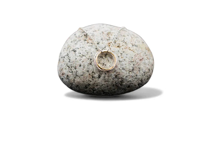 The Lynsey de Burca Doorus Mix Pendant is shown draped over a smooth, speckled gray stone with a white background.