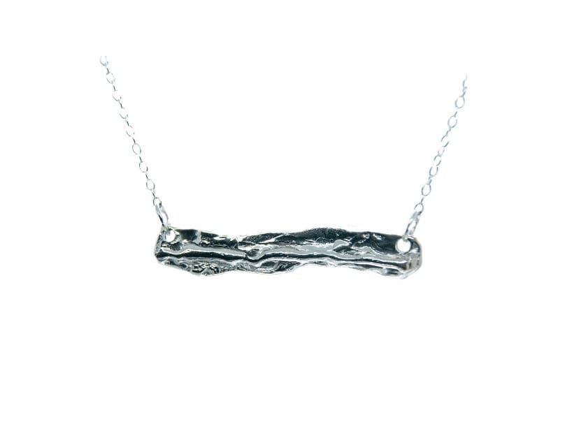The Driftwood Silver Pendant by Ava Jane Jewellery features a textured sterling silver bar on a thin chain, inspired by driftwood from Dublin Bay. Shown against a plain white background.