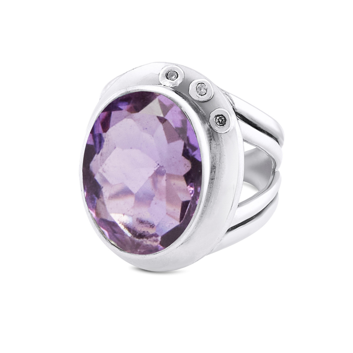 The Eyetelia Ring by Gallardo & Blaine Designs is a statement cocktail ring in sterling silver with an oval-cut purple gemstone center, accented by three small round diamonds on the band.