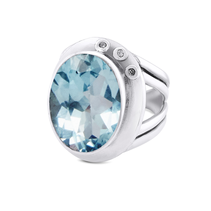 The Eyetelia Ring by Gallardo & Blaine Designs features a large oval-cut light blue gemstone accented by three small clear stones, set on a sterling silver gold vermeil band.