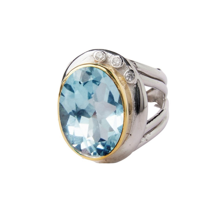 The Eyetelia Ring by Gallardo & Blaine Designs features a large oval blue gemstone with three round diamonds above it, crafted in sterling silver gold vermeil and shown on a white background.