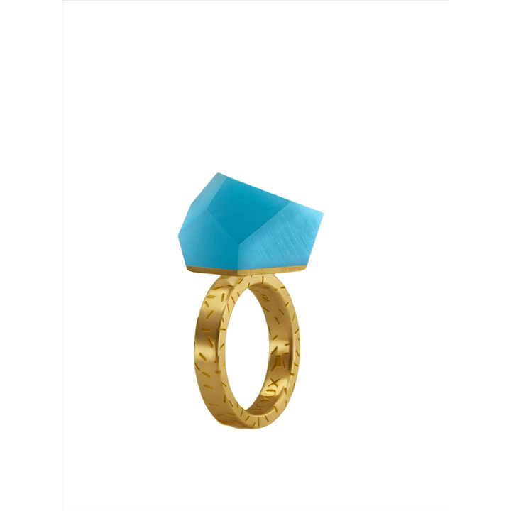The Fruit Bijoux Ring Top VU Crystals Capri Blue by Fruit Bijoux features a textured 24ct gold-plated band with a large, angled geometric blue gemstone, shown against a plain white background.