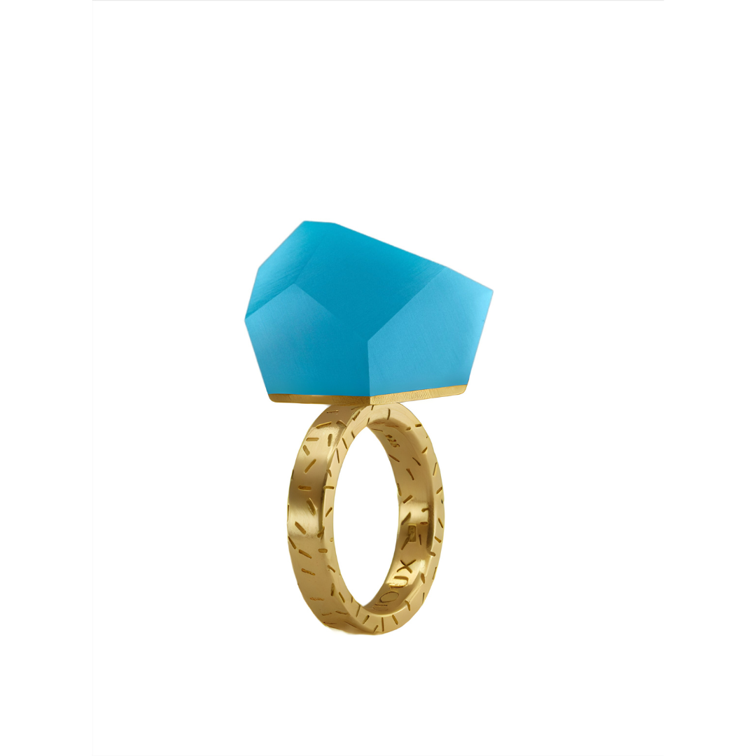 The Fruit Bijoux Ring Top VU Crystals Capri Blue by Fruit Bijoux features a textured, engraved gold-plated band and a bold geometric Capri Blue gemstone, shown against a white background.