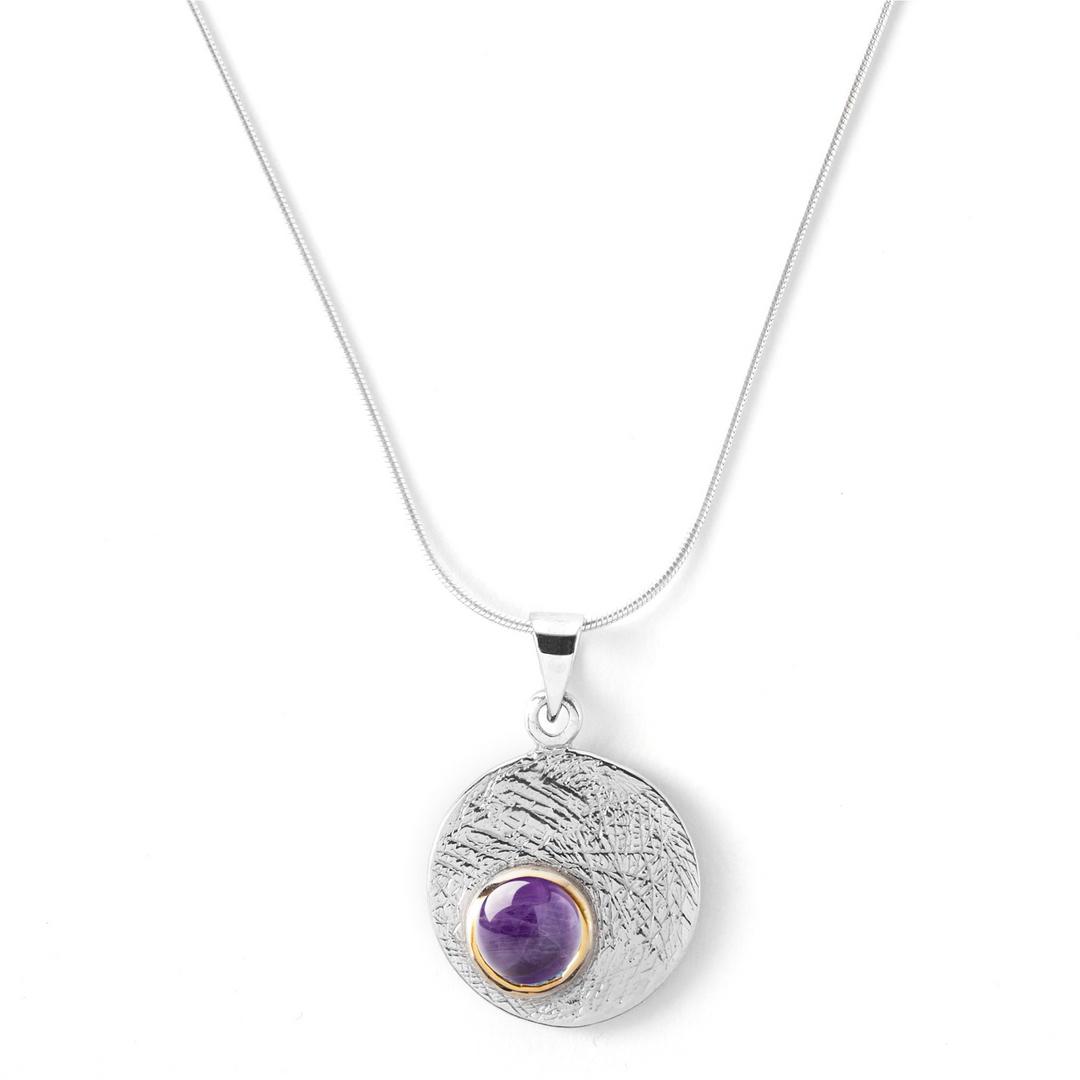 The Selene Necklace Silver - Small by Gallardo & Blaine Designs features a textured sterling silver round pendant with a central purple gemstone and gold border, shown on a white background—an elegant, customizable piece.
