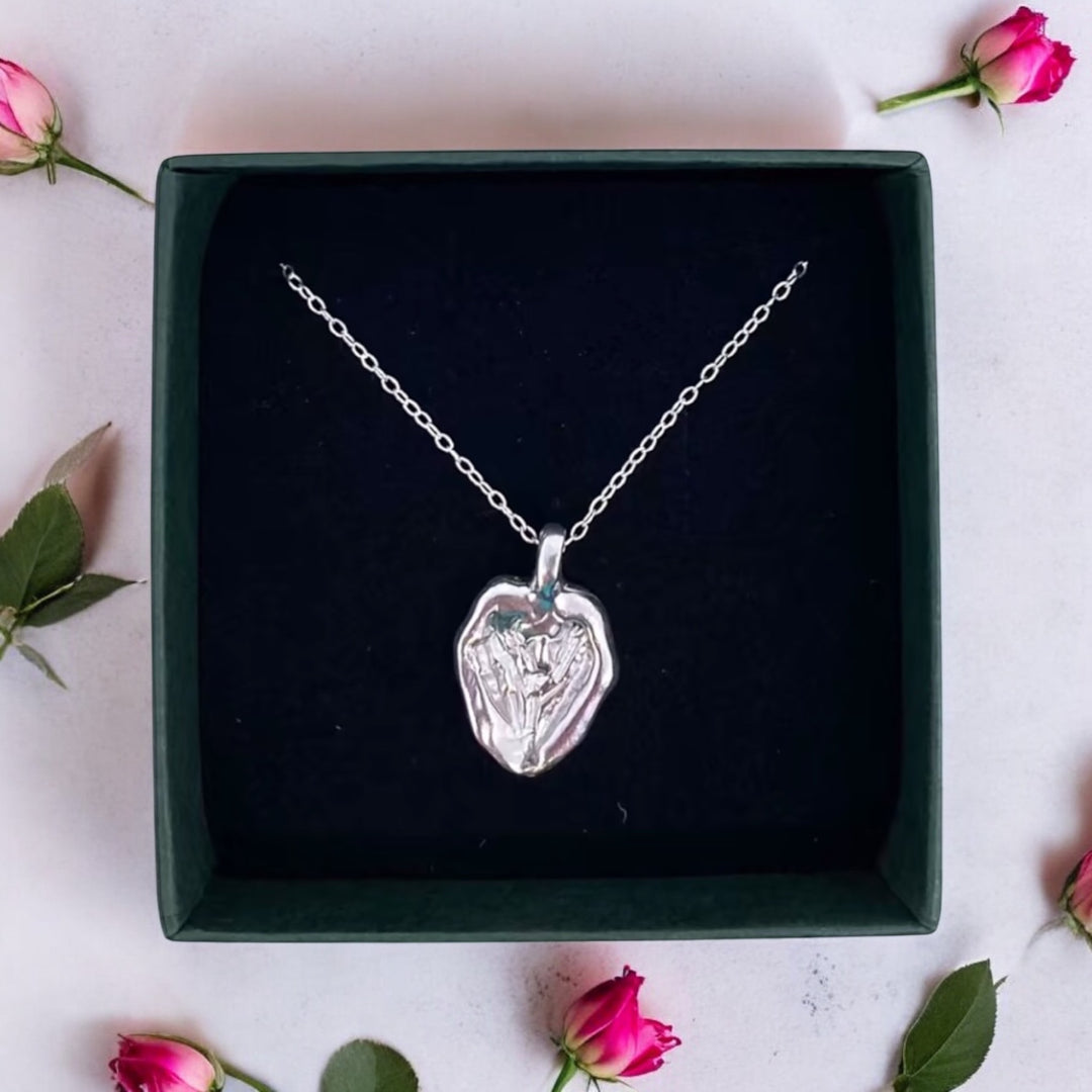 The "You Melt My Heart Silver Pendant" by Ava Jane Jewellery is shown in a black box, accented with pink rosebuds and green leaves on a light surface.