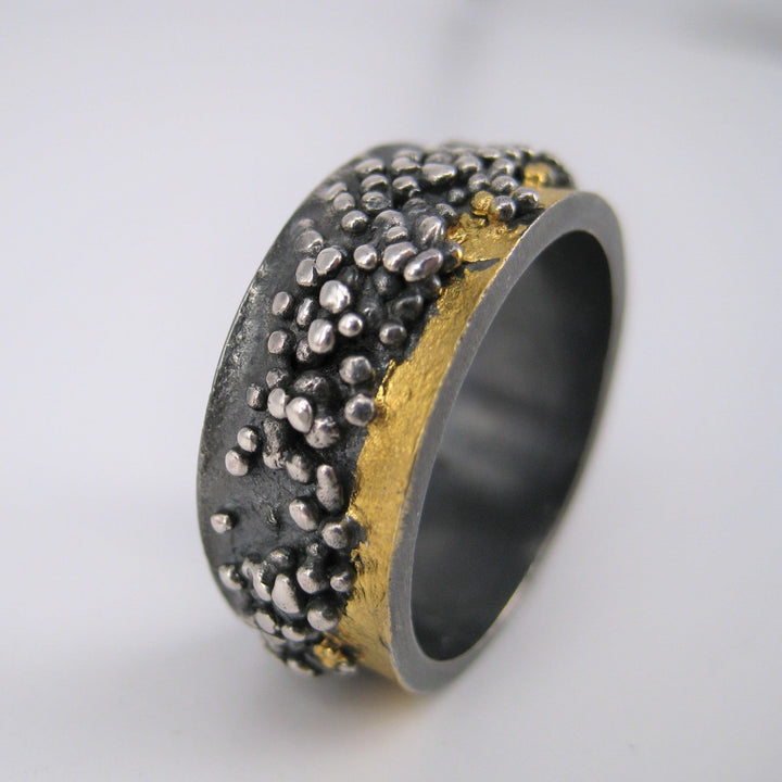 The Wide Etrusc Ring by MarCucurella features a textured wide band with silver bead clusters inspired by Etruscan granulation and a gold kumboo accent, offering a striking contrast between rough and smooth finishes.