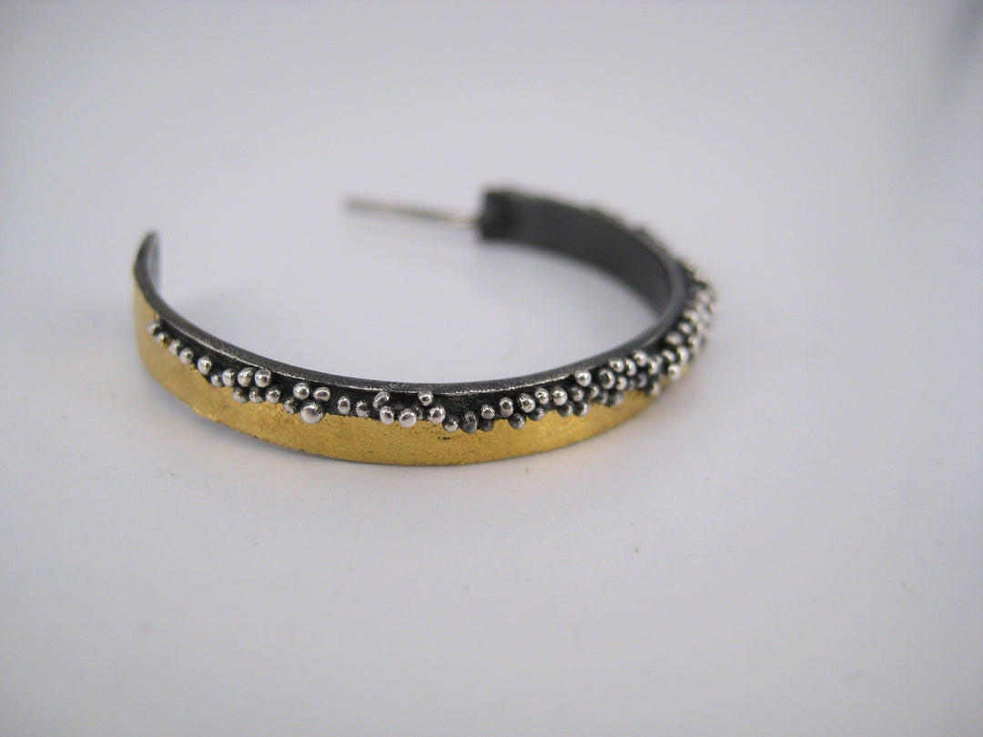 A close-up of MarCucurella's Etrusc Hoop Earrings in various sizes shows a gold band accented with small silver beads along the top edge, set against a plain white background.