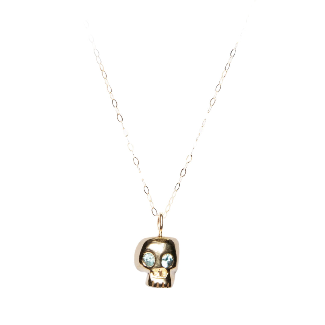 Introducing the Cosmic Boulevard 9ct Gold Memento Mori Skull Pendant, expertly crafted in our Dublin Studio. This delicate gold necklace features a chain of oval links and a pendant adorned with a small, stylized skull design. The eyes are set with blue gemstones, adding a unique touch to this exquisite piece against a plain white background.