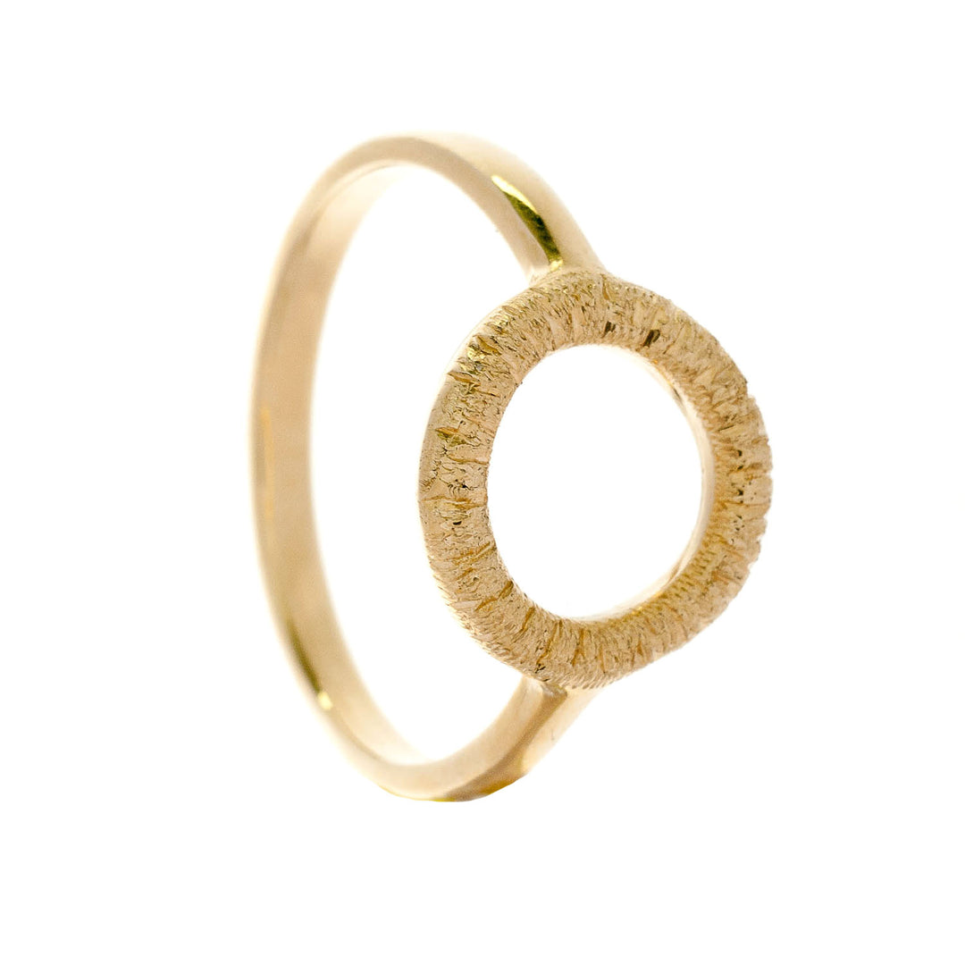 An Into The Light Mini Ring 9ct Yellow Gold with a thin, polished band and an open circle design as the centerpiece. The circle has a textured, brushed finish that contrasts with the smooth band, reflecting the coastal textures of Ireland. This piece is lovingly handmade in Audrey’s home workshop and is part of her Aud ring collection.