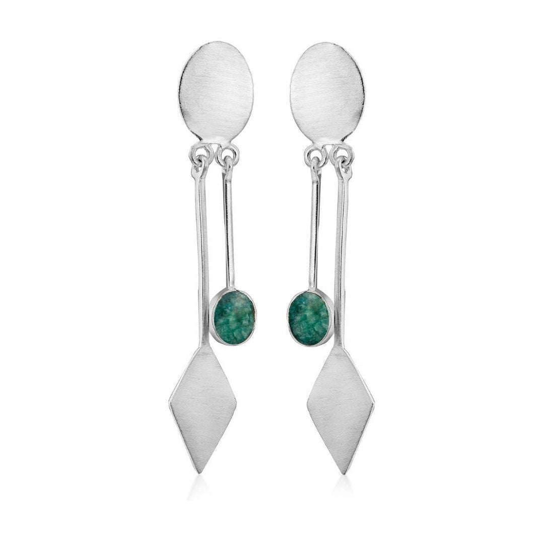 The Karo Earrings by Gallardo & Blaine Designs showcase modern elegance with an oval stud, a kite-shaped charm, and a green stone on a thin dangling silver chain, highlighting their sophisticated allure. Available in various gemstones.