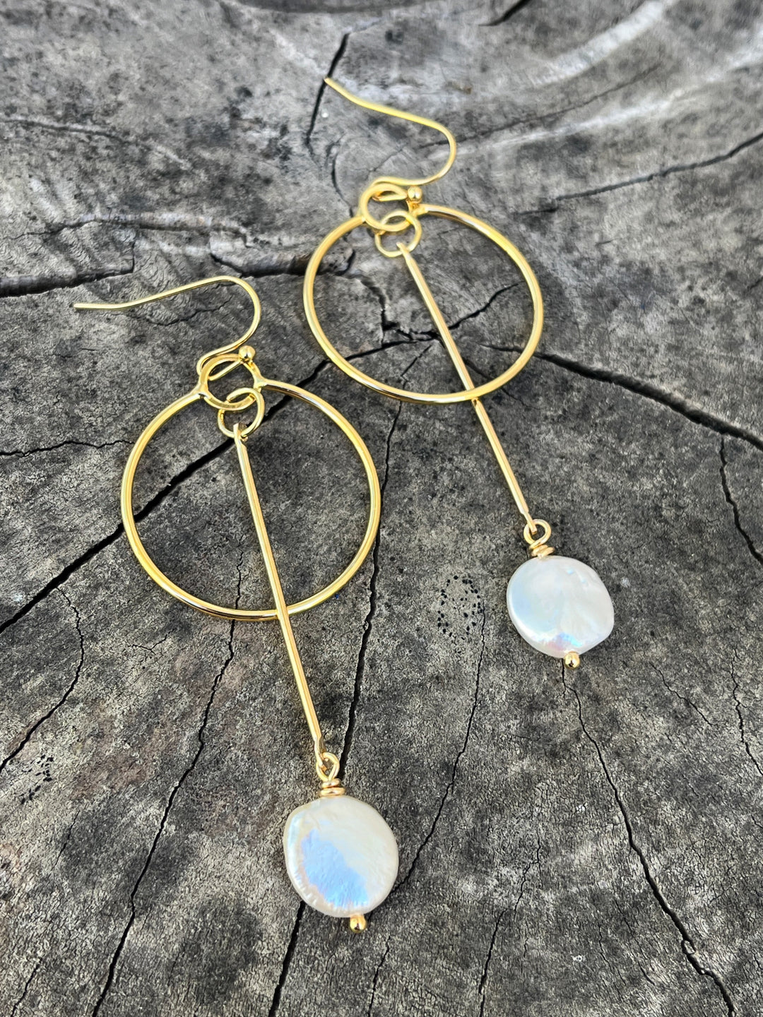 The Kea Earrings with Freshwater Pearl Drops by Kybalion Jewellery feature gold-plated hoops with vertical bars and iridescent pearls, beautifully displayed on textured gray wood—elegant handmade Dublin jewelry.