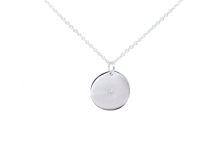 The Personalised Charms Hand-stamped Initial Necklace is a gold plated sterling silver piece with a delicate chain and a round, engraved "K" pendant. This customizable necklace is displayed against a white background.