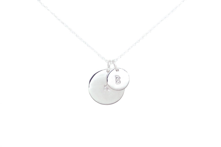 The Hand-stamped Initial Necklace by Personalised Charms features two pendants—a plain larger disc and a smaller one hand-stamped with your chosen initial—crafted in timeless sterling silver for any occasion.
