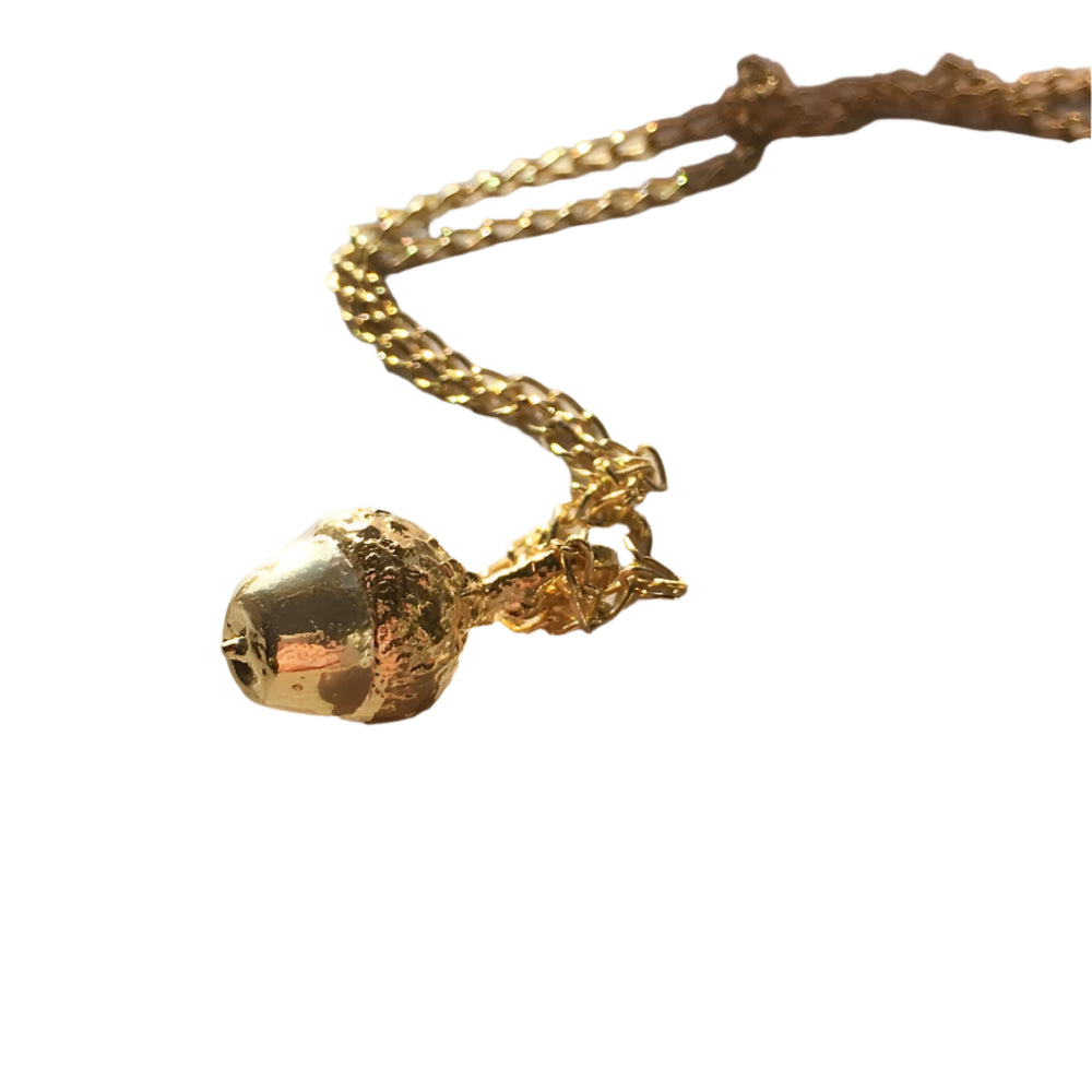 The Little Acorn Necklace Gold by Andrea Mears Jewellery showcases a shiny, textured gold-plated acorn pendant on a delicate chain, beautifully presented against a white background.