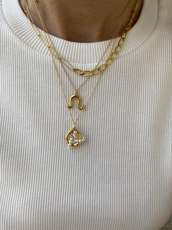 Close-up of a person wearing a ribbed white sweater, showcasing the Mixed Links Necklace by Bonvo. The top chain necklace has a simple design, the middle one features a unique squiggle pendant, and the bottom necklace has a pendant with a pearl encased in gold setting.