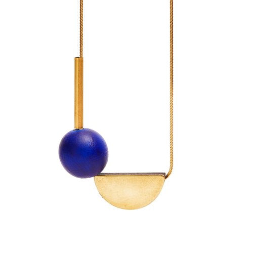The Shock of Grey Multishape Necklace in Blue features a handcrafted gold chain with a vertical gold bar, round blue bead, and semicircular pendant in a geometric design—made in Dublin and shown on a white background.