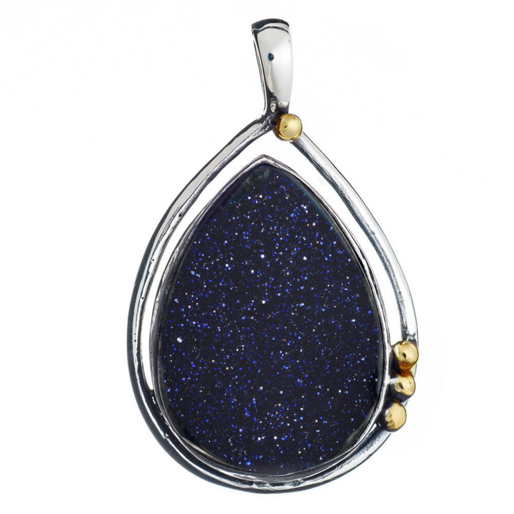 The Poppy Pendant Large by Gallardo & Blaine Designs features a teardrop-shaped sterling silver frame with a dark blue glittering gemstone, accented with gold beads on the side and top.