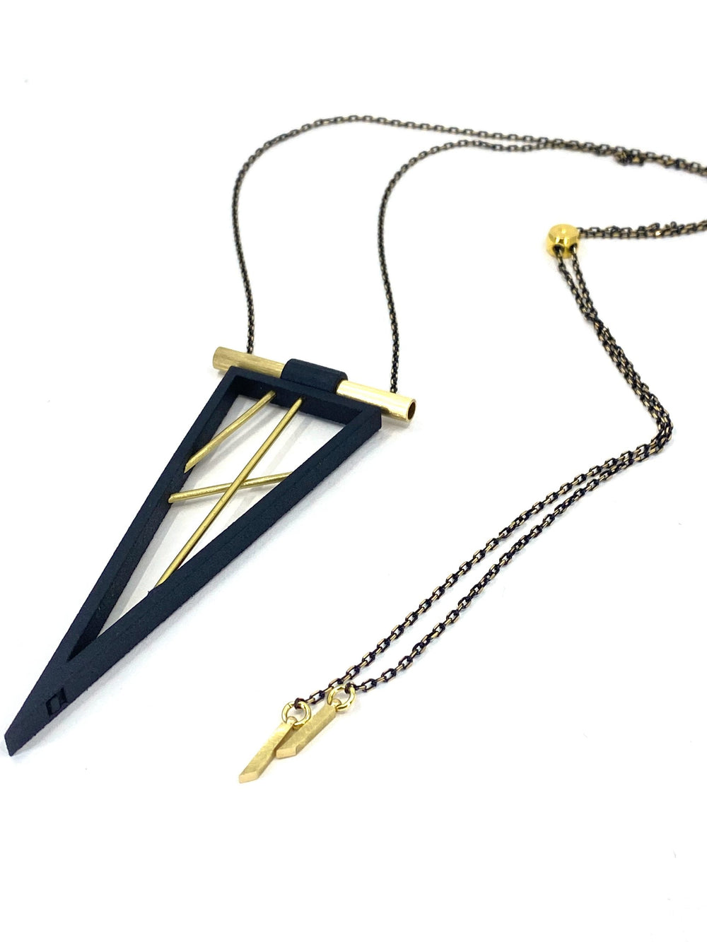 The Elsiem Rapture Spear Long Chain Necklace showcases a geometric pendant with a black triangular frame, abstract gold bars, and is finished with a gold chain and a small charm at the clasp.