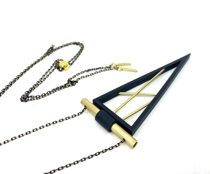 The Elsiem Rapture Spear Long Chain Necklace is a modern neckpiece featuring a black triangular pendant with gold accents on a dark chain and gold clasp, shown against a white background.