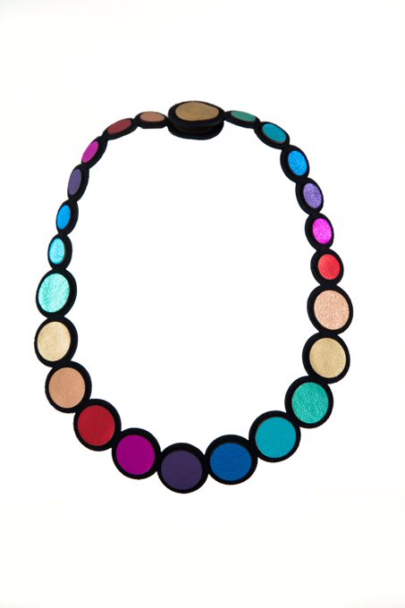 The Rainbow Leather Necklace by Iskin Sisters features a gradient pattern of beads in various colors, including shades of blue, pink, purple, and gold, with each bead encircled by a thin black border. Its lightweight design makes it perfect for everyday wear.