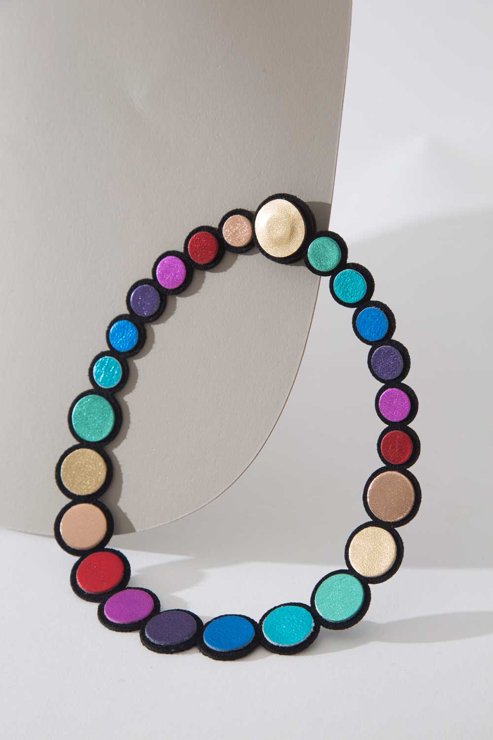 A vibrant Rainbow Round Leather Necklace from Iskin Sisters rests elegantly on a white surface, featuring an Argentinian leather strap and a lightweight design.