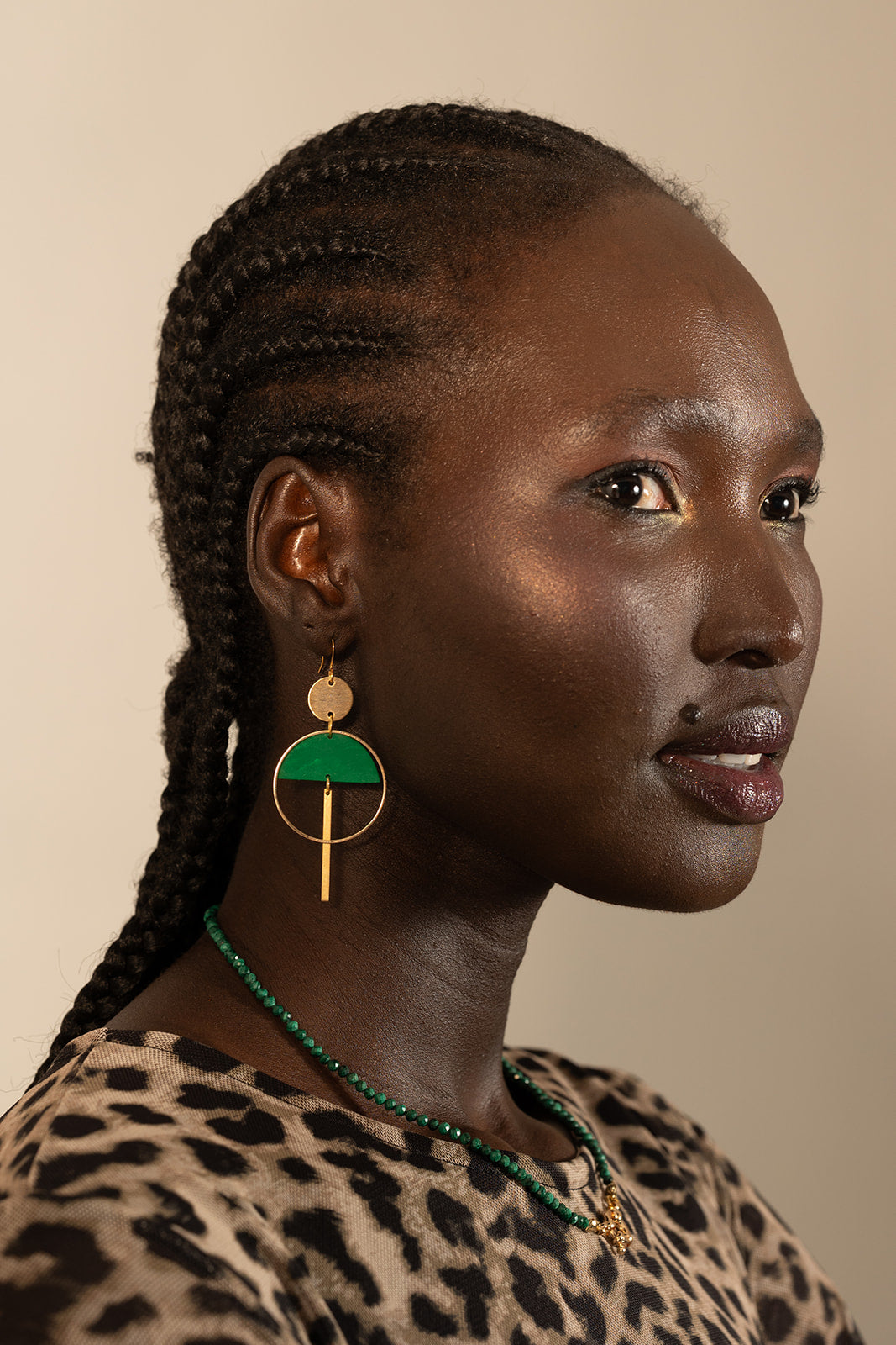 A woman with braided hair models Kybalion Jewellery's Sinead Earrings in various colours, paired with a leopard-print top and green beaded necklace, as she gazes sideways against a neutral backdrop.