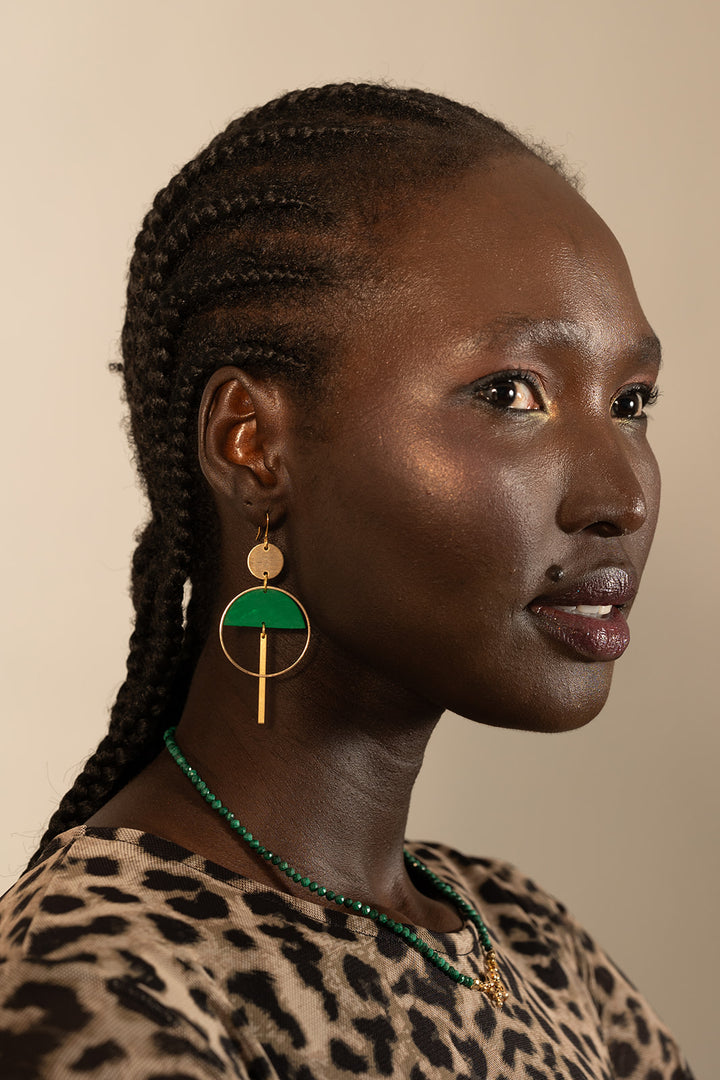 A woman with braided hair models Kybalion Jewellery's Sinead Earrings in various colours, paired with a leopard-print top and green beaded necklace, as she gazes sideways against a neutral backdrop.