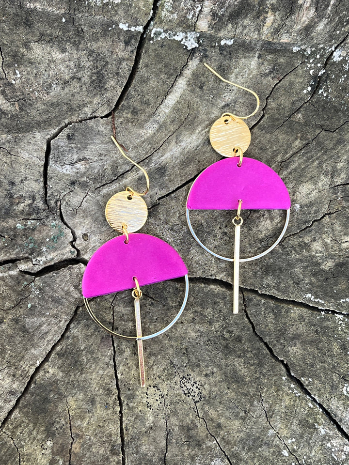 The Sinead Earrings by Kybalion Jewellery, shown in gold plating on a textured tree bark, feature vibrant colors with a bright pink polymer half moon, gold circle, large hoop, and vertical bar drop.
