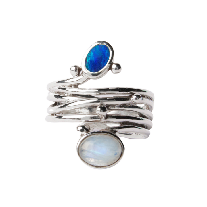 The Snake Ring in Silver by Gallardo & Blaine Designs features a textured, adjustable band with two bezel-set oval gemstones—deep blue and iridescent white—and delicate silver bead accents.