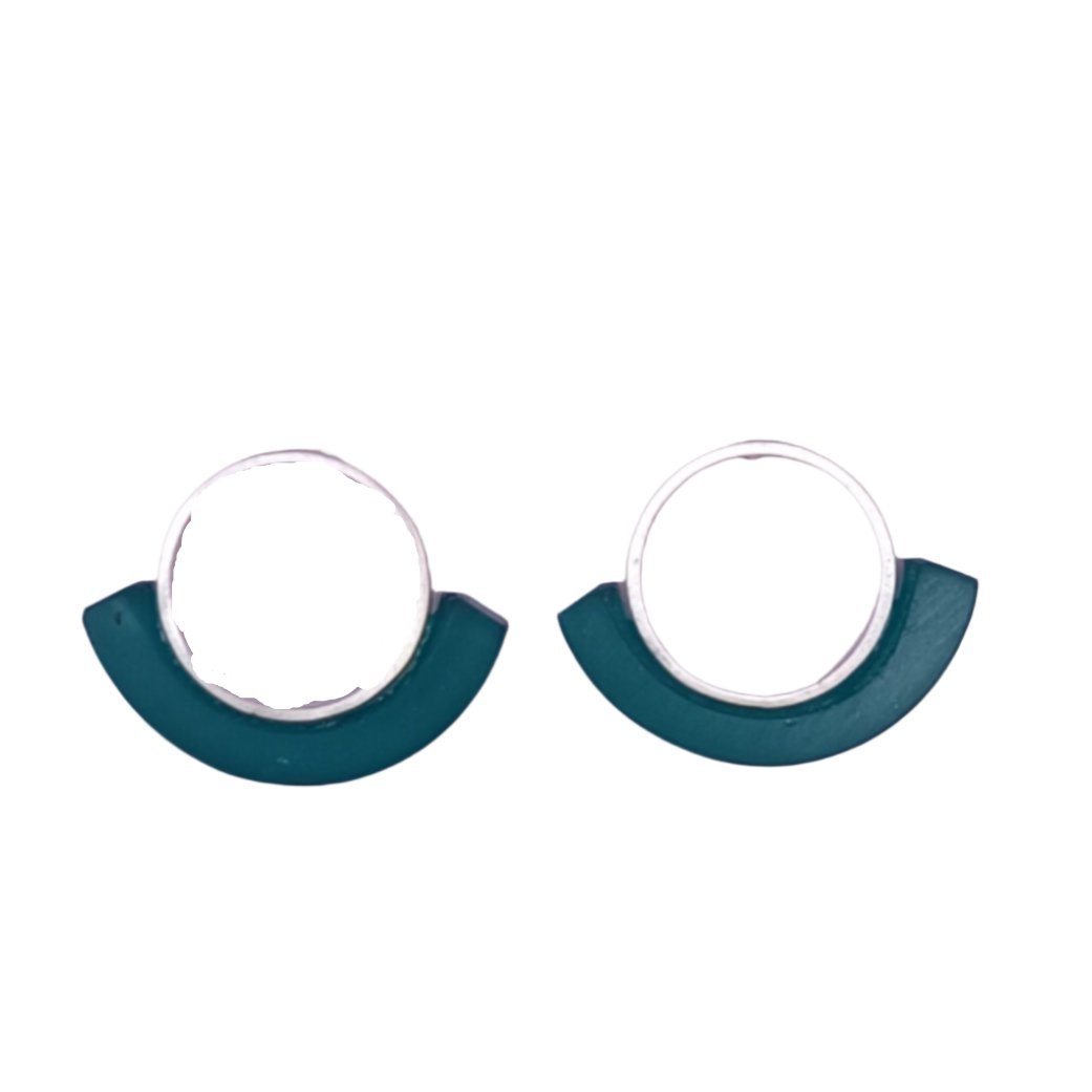 A pair of Soul Colours Medium Silver Short Earrings in teal, crafted by Beira by Irene Reyes, are displayed on a light pink card labeled "BEIRA," resting on a white surface. Part of a dark green bracelet with yellow accents is visible at the top of the image.