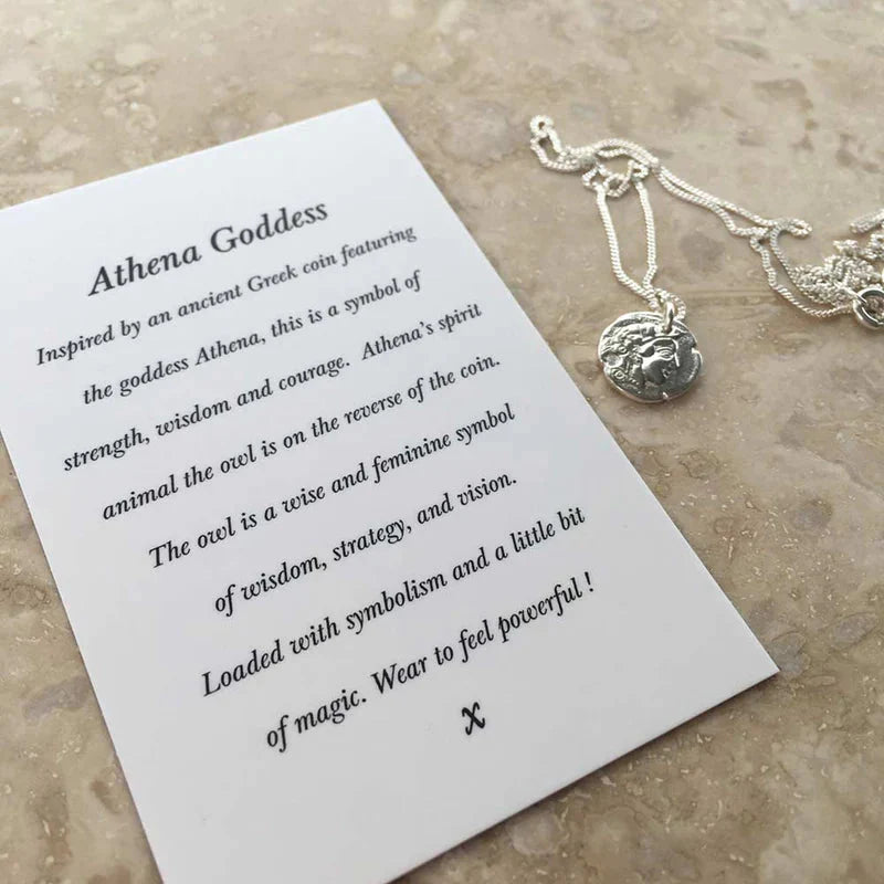 The Athena Coin Necklace Silver by Andrea Mears Jewellery, featuring an Athena pendant, rests on marble next to an "Athena Goddess" card highlighting the owl as a symbol of wisdom, strategy, and magic. Inspired by ancient Greek coinage.