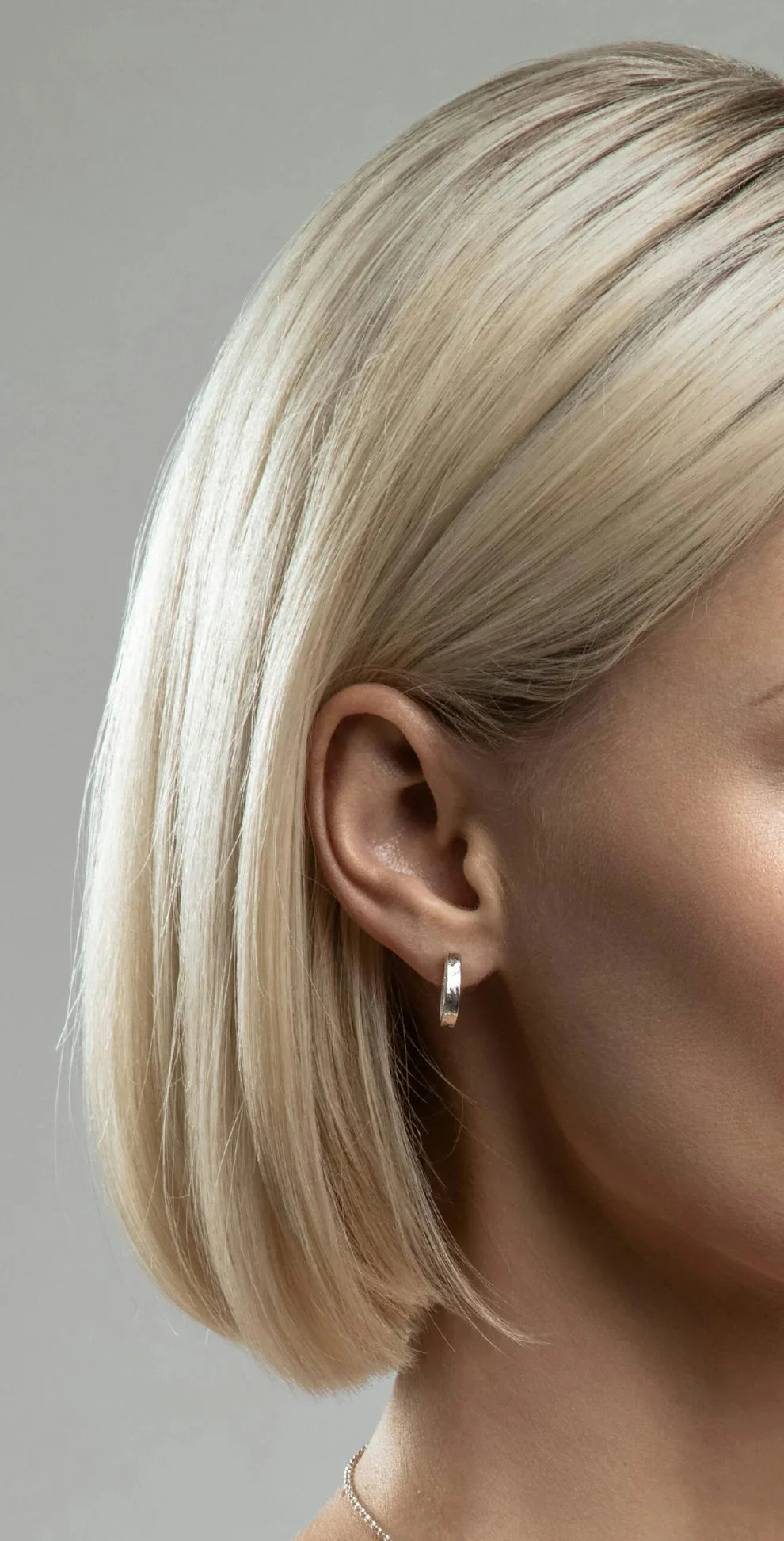 Close-up of a person with a straight, platinum blonde bob wearing Lynsey de Burca's Talún Studs in sterling silver, set against a plain gray background.
