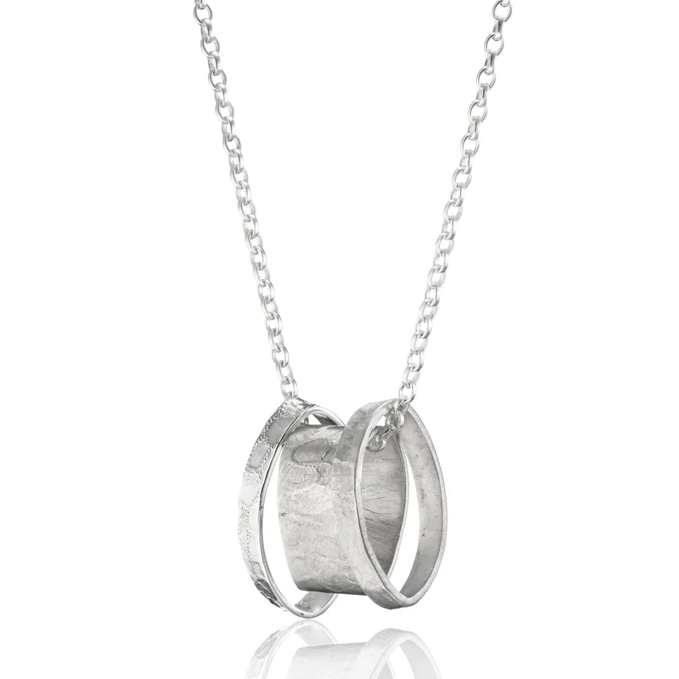 A sterling silver chain necklace featuring three interlocking rings. The rings are different sizes and have a polished, metallic finish. The largest ring has a wider band, while the other two rings are thinner. This handmade jewellery piece showcases a minimalist and modern design.
Introducing the Talún Triple Neckpiece by Lynsey de Burca.