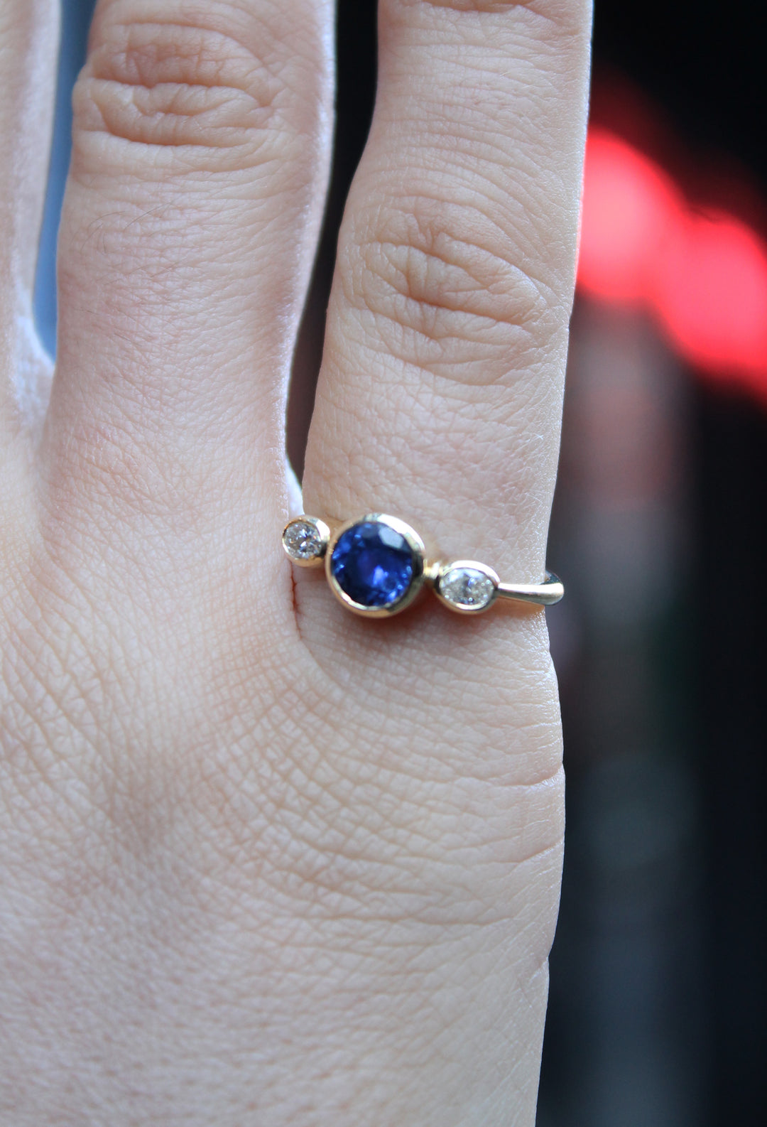 18ct yellow gold ring with round sapphire in the centre and an oval shaped diamond on either side. The band is tapered to a D shape, the band is widest at the back at 2.3mm and becomes thinner towards the front of the ring. Shown here on a pinky finger.