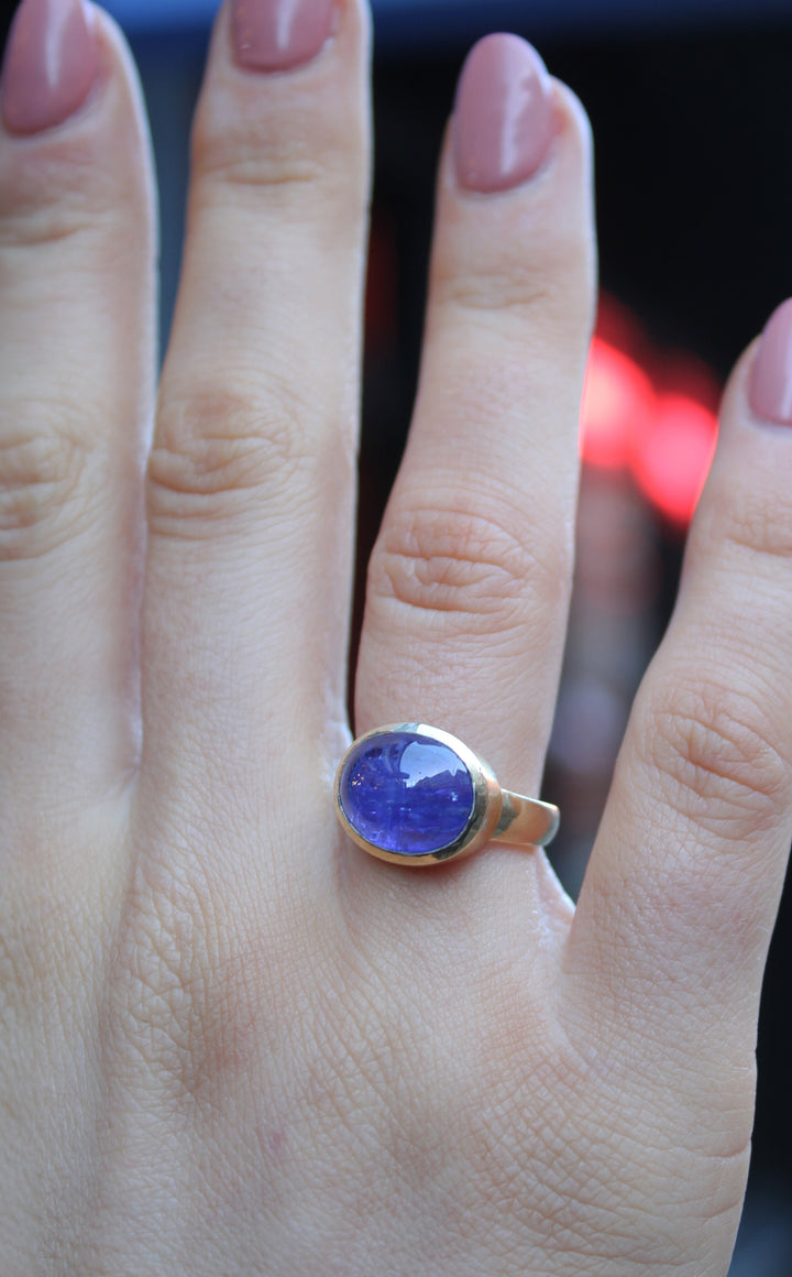 9ct Yellow gold ring with a large oval cabochon Tanzanite, which is a dark blue purple colour. The 9ct yellow gold band is D shaped with the widest at the back at 3mm. Shown here on a ring finger